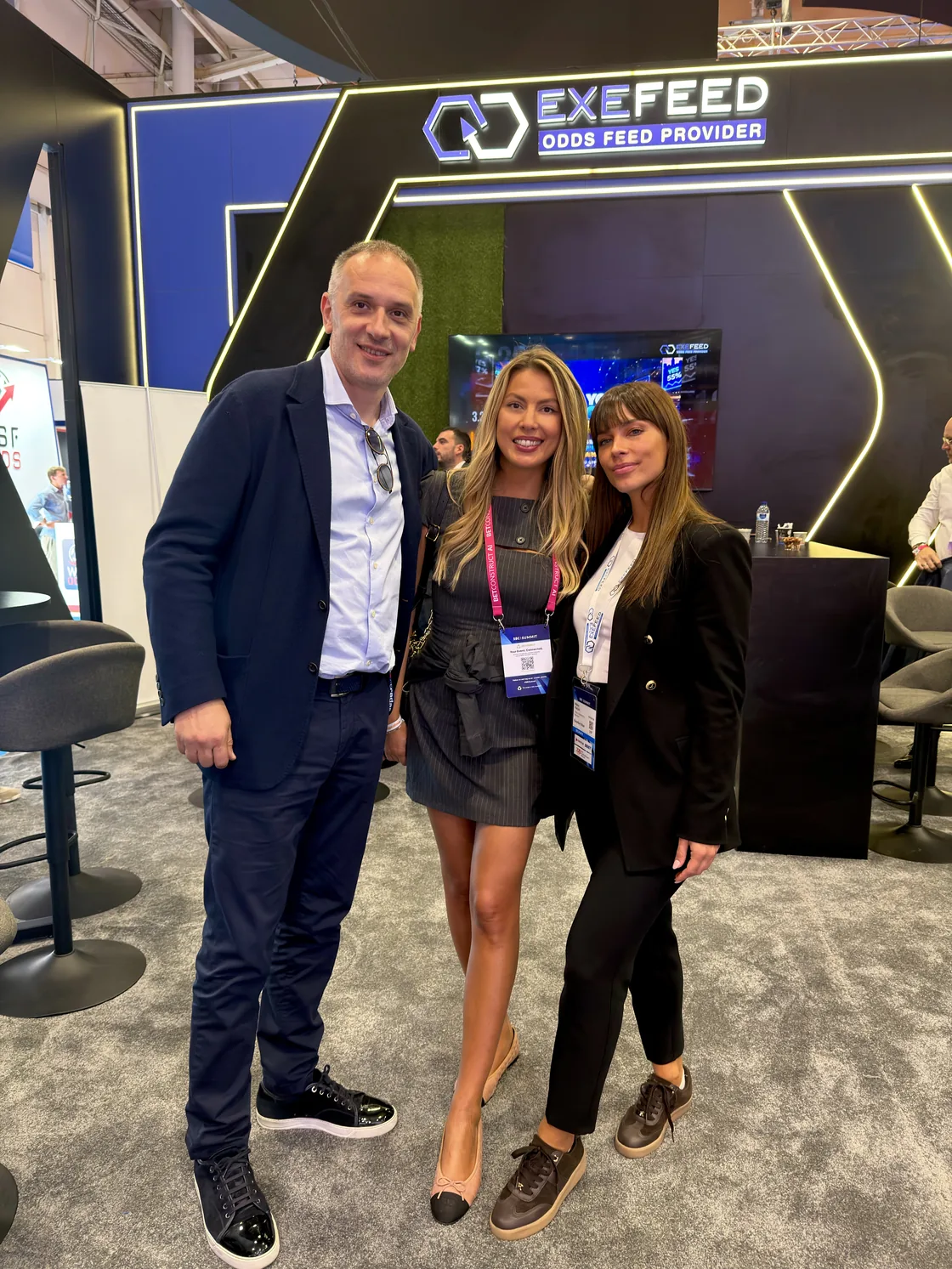 Three people photographed together in front of the stand
