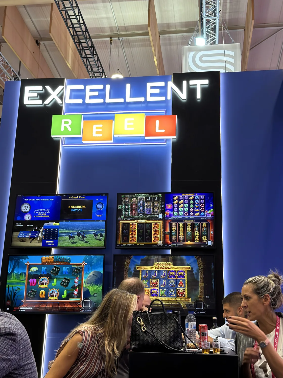 Visitors seated in front of the screens, beneath the Excellent Reel logo wall